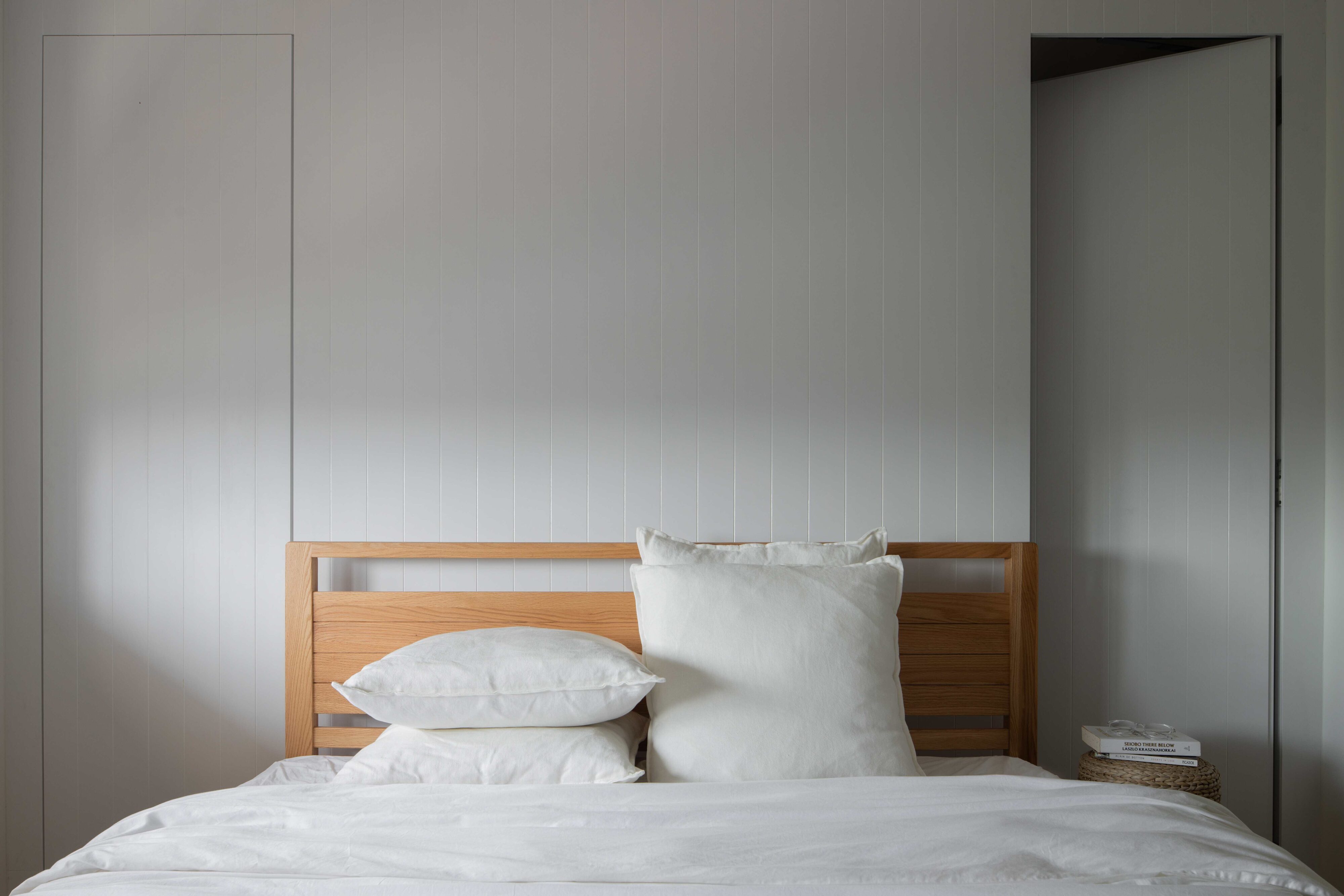scandinavian bedroom with teak slatted headboard, crisp white bedding and vertical panel walls bathed in soft natural light.
