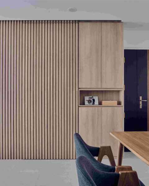 Compact dining area defined by full-height fluted timber feature wall with concealed storage and doorway