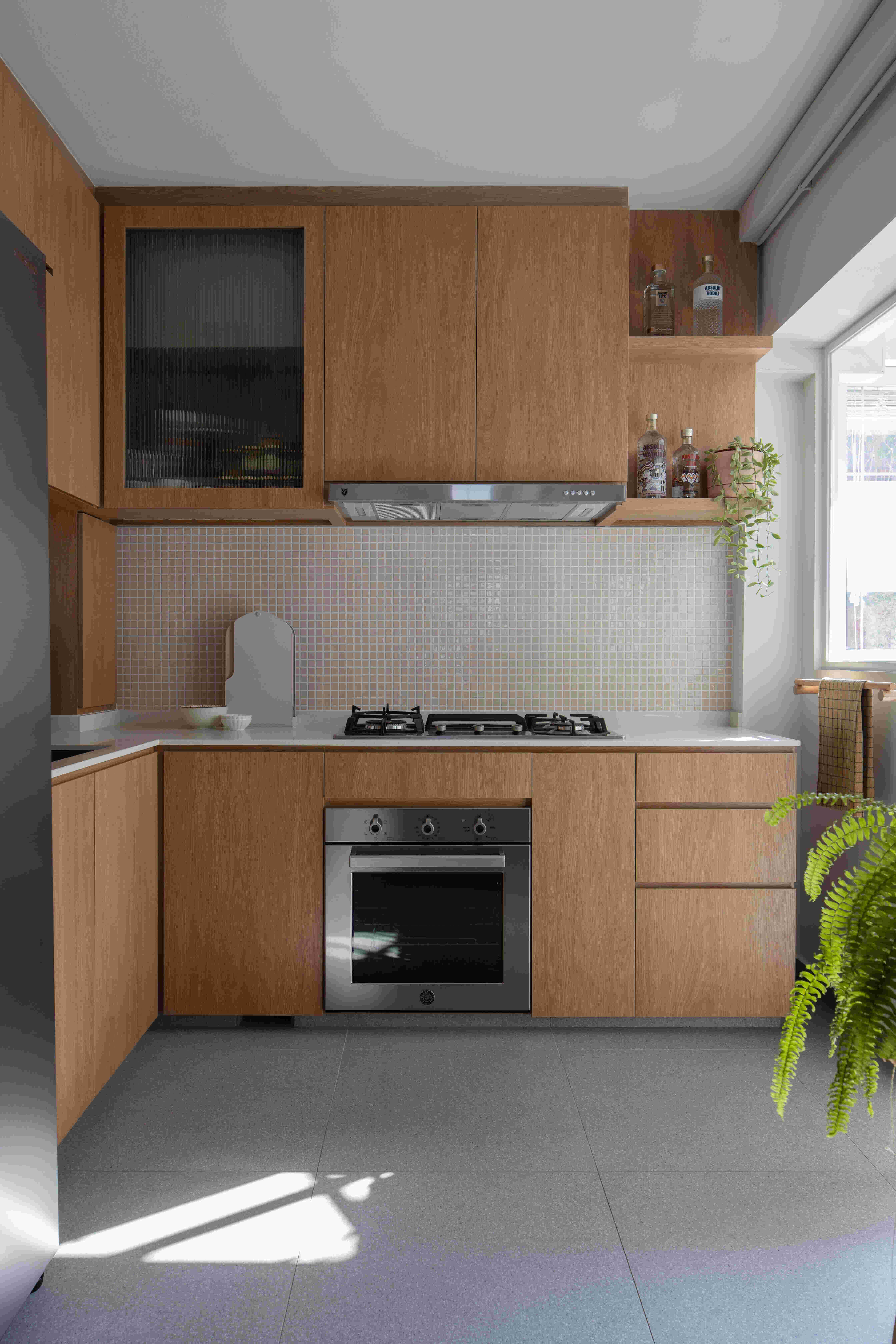 Small kitchen design with L-shaped light-wood cabinets, gas hob, built-in oven, mosaic tile backsplash and window herb planter