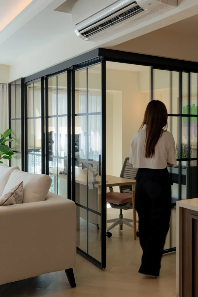 HDB multipurpose room with sliding black-framed glass partition forming a bright home office beside living area