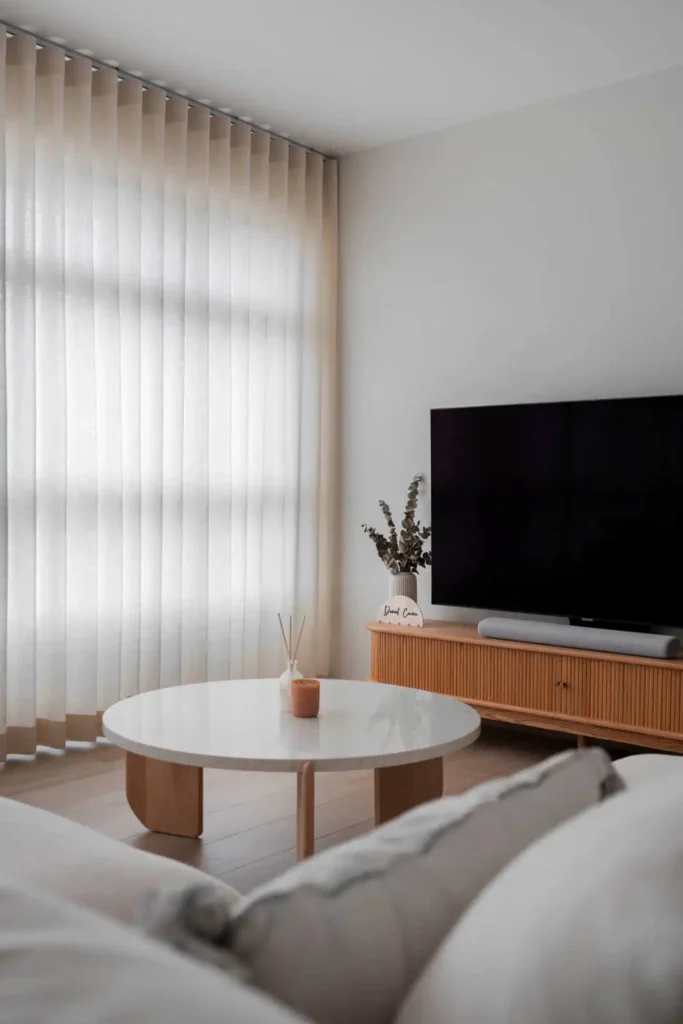 Soft minimalist living room with ripple-fold sheer curtains, round white coffee table and fluted TV console