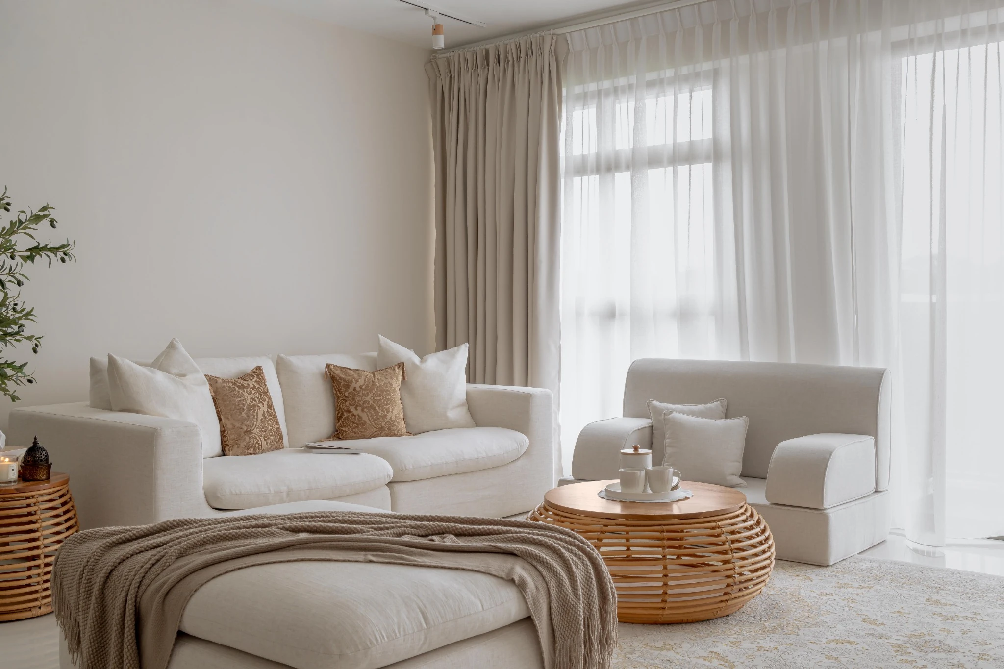 Neutral living room with a light sofa set, rattan coffee table, and sheer curtains filtering daylight.