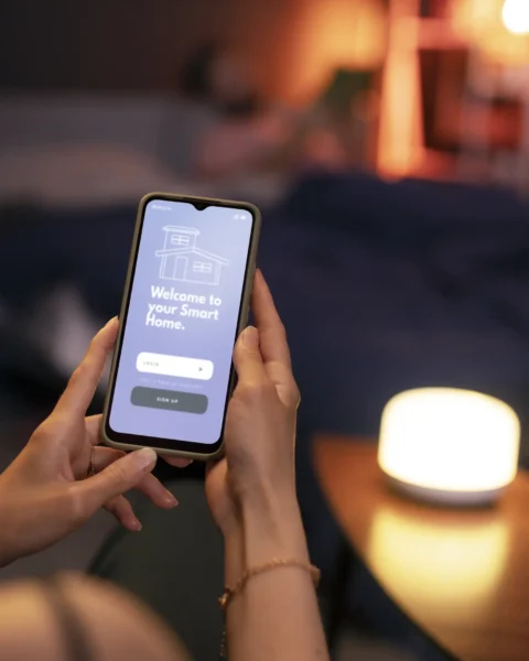 Renter uses a phone app to dim a bedside smart lamp in a cozy bedroom—no wiring or drilling needed.