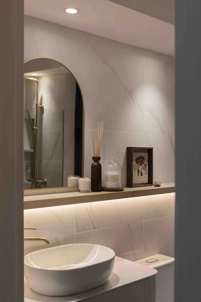 Scandinavian bathroom with arched mirror, brass tapware and a backlit ledge in a warm minimalist palette.