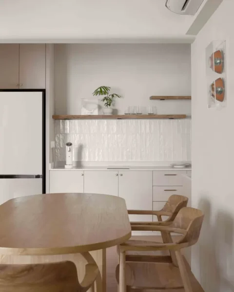 Minimalist Scandinavian kitchen with white tiled backsplash, open wood shelves and a light-wood dining set.