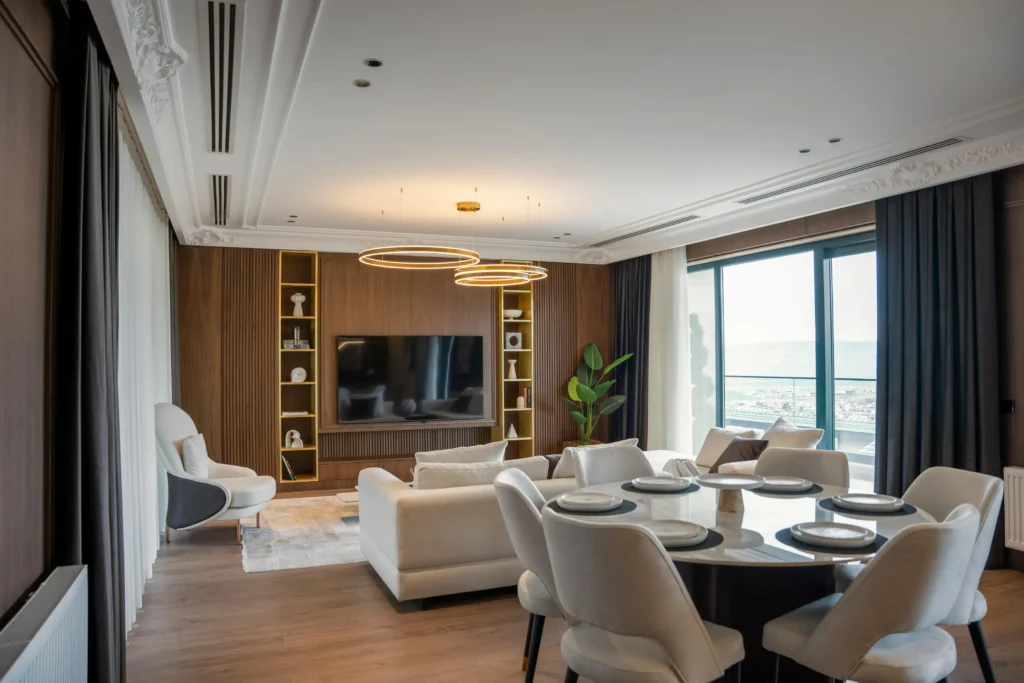 Modern living–dining room with smart ring pendant lighting, scene control, and layered curtains beside a large window, styled in warm wood tones.
