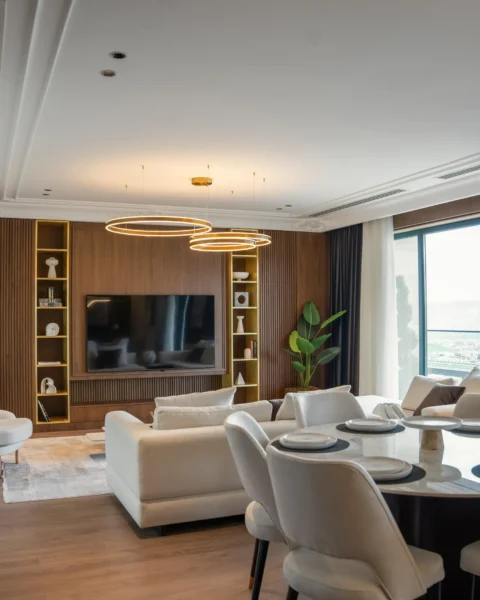 Modern living–dining room with smart ring pendant lighting, scene control, and layered curtains beside a large window, styled in warm wood tones.