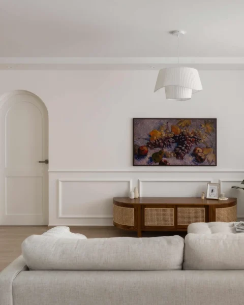 Bright living room with an arched door, wall moulding, rattan-front console, and framed artwork above.