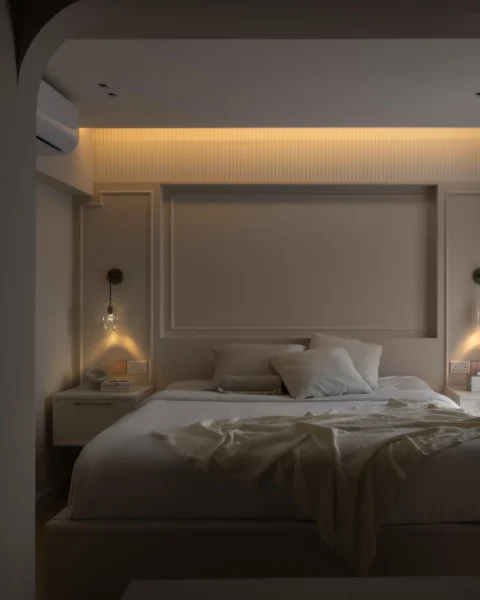 Cozy bedroom framed by an arched opening, with warm cove lighting, bedside sconces, and layered neutral bedding.