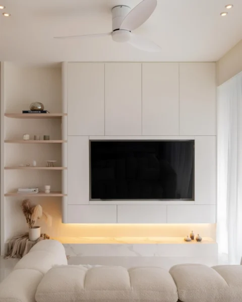 Minimalist TV feature wall with built-in cabinetry, open shelves, and warm cove lighting near sheer curtains.