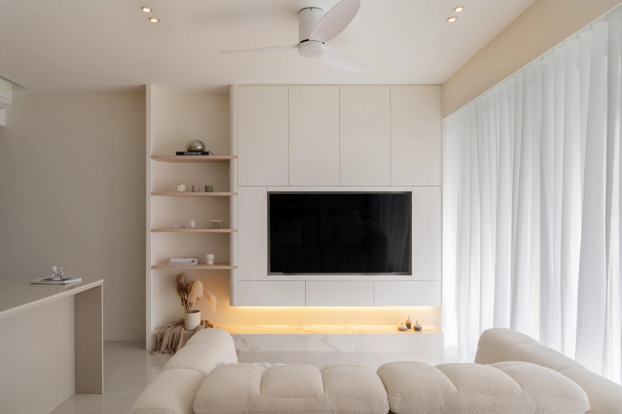 Minimalist TV feature wall with built-in cabinetry, open shelves, and warm cove lighting near sheer curtains.