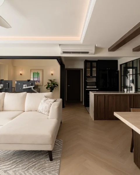 Open-plan living and dining space with a neutral sectional, dark kitchen cabinetry, and a herringbone wood floor.
