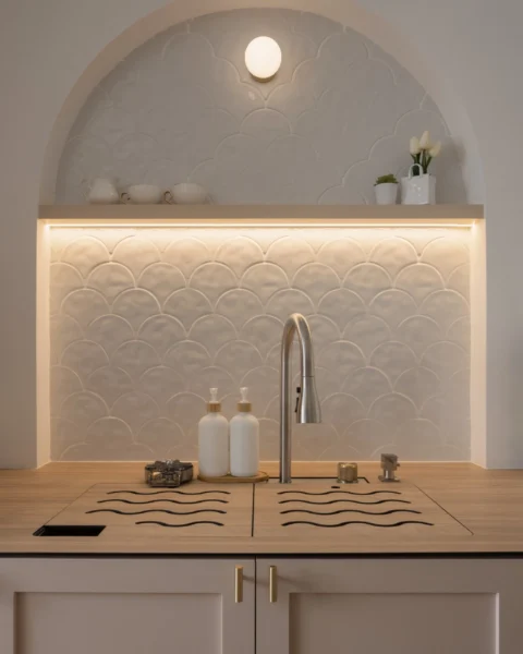 Kitchen sink with an arched niche, scallop-tile backsplash, under-shelf lighting, and simple countertop accessories.