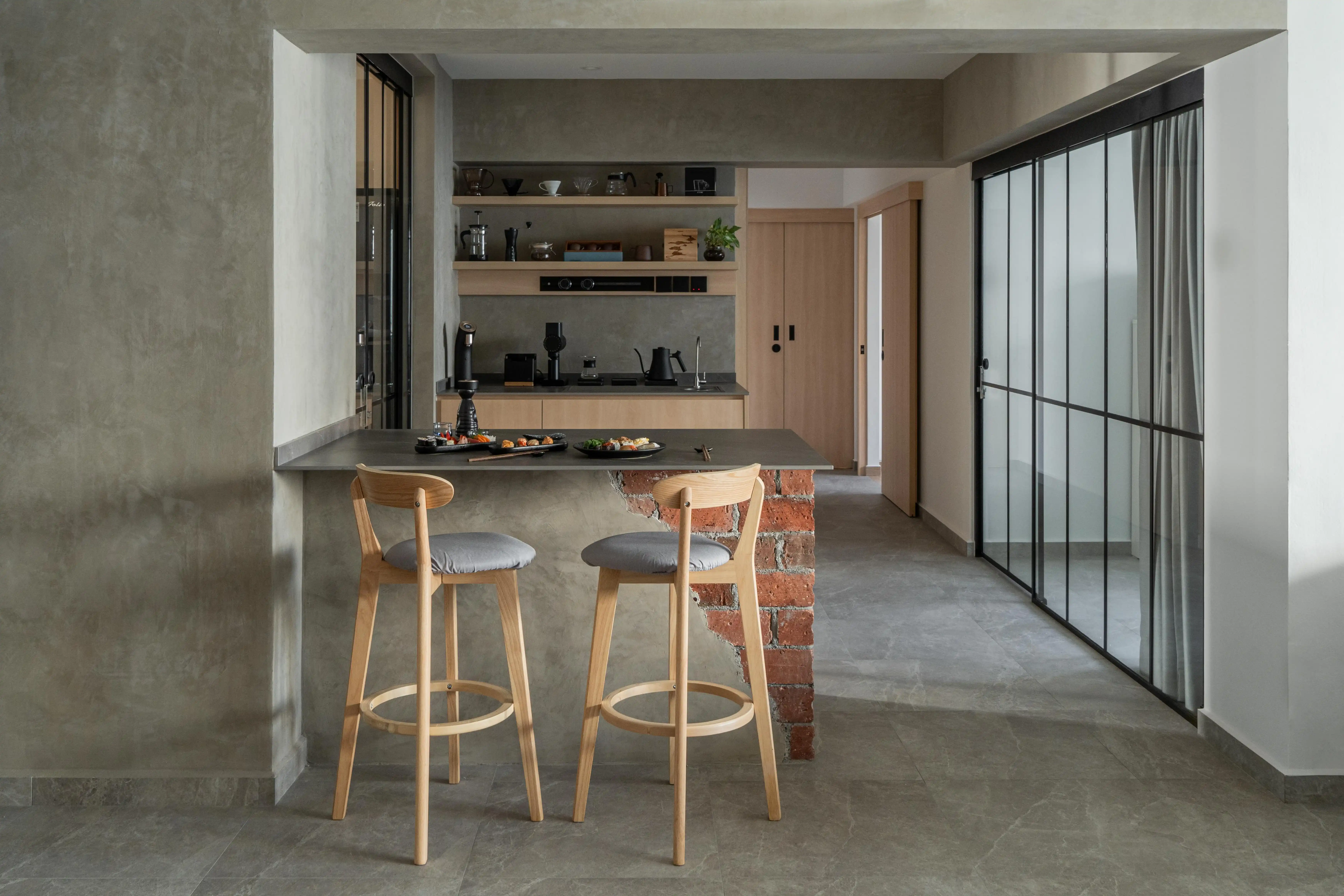 Industrial Muji kitchen bar with concrete-look walls, exposed brick island, minimalist open shelves, and black-framed sliding glass doors.