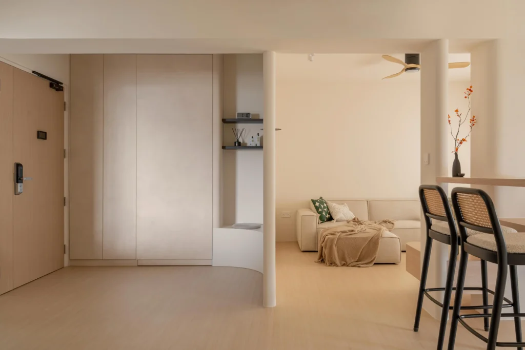 Minimal open-plan living space with pale timber flooring, white walls, built-in entry storage, and bar counter seating.