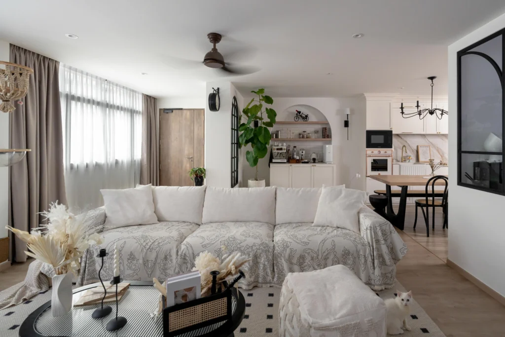 Bright living room with a cosy sofa, arched coffee nook, classic white kitchen cabinets, and black-framed glass doors.