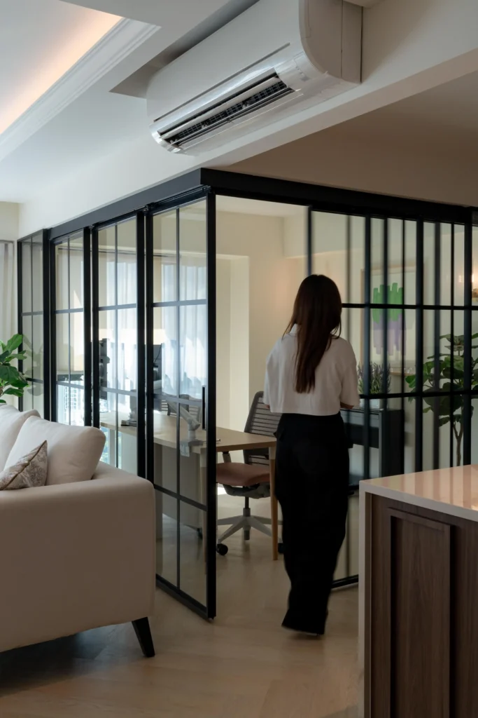 Home office separated by a black-framed sliding glass partition within an open living space.