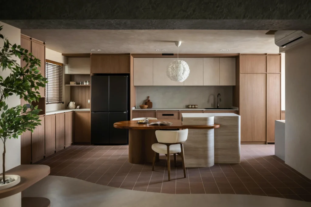 Warm wood kitchen with a rounded stone island, pendant lights, and terracotta tile flooring.