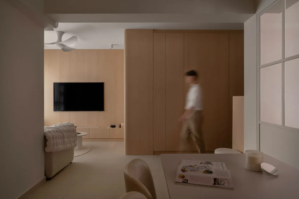 Open-plan living room with a wall-mounted TV on a light wood panel and a ceiling fan.