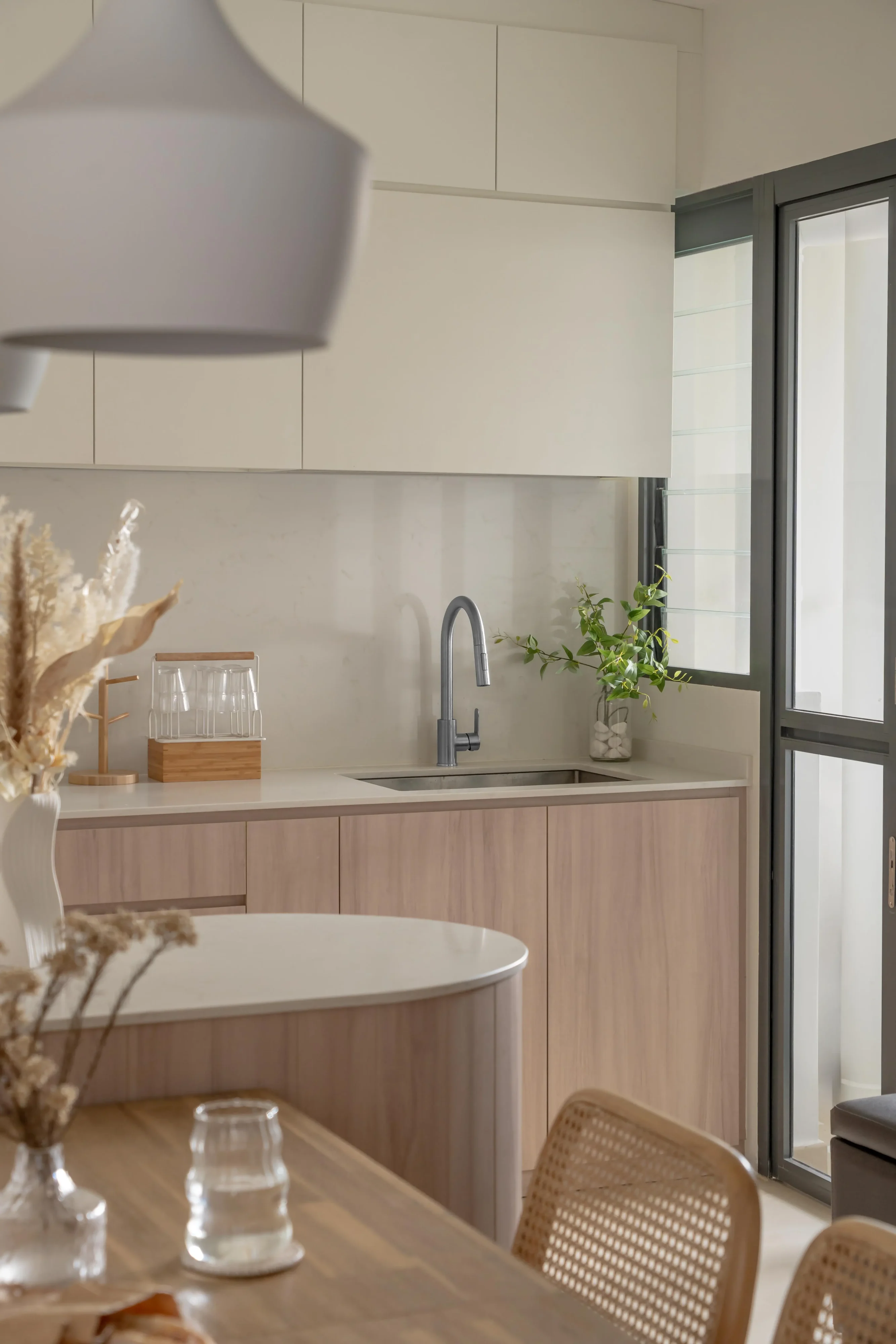 Modern Japandi interior design featuring light wood kitchen cabinets, a curved island, and minimalist decor under soft warm lighting.